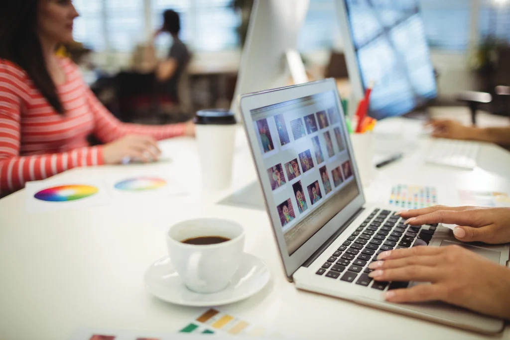 Graphic designers working on their laptops with color palettes and a cup of coffee on the desk.